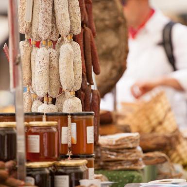 Mercato vivace con salumi appesi e vasetti di miele, atmosfera rustica e profumi intensi.